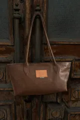 Cartera tipo tote de tamaño mediano, confeccionada en cuero con pelo con un diseño estampado de manchas en tonos marrones. Posee doble asa de hombro en cuero liso marrón y cierre superior.