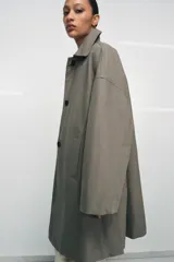 Trench oversize de Zara Woman Collection, confeccionado en hilatura de algodón. Presenta cuello solapa, manga larga, bolsillos delanteros y cierre frontal con botones ocultos bajo solapa.