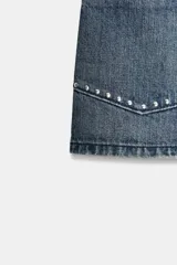 Shorts de jean tiro medio con bolsillos delanteros de plastrón decorados con tachas metálicas. Presenta cierre frontal con cremallera y botón metálico.