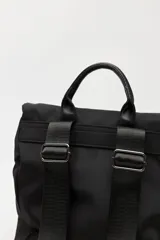 Mochila urbana de nylon color beige, con solapa superior, bolsillo frontal con cierre y correas decorativas con hebillas metálicas. Incluye manija superior y correas ajustables.