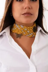 Gargantilla tejida a mano en crochet con diseño entrelazado en tonos mostaza y gris. Presenta un dije metálico en forma de mariposa y detalles ornamentales oscuros, ofreciendo un estilo artesanal y sofisticado.