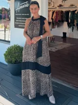 Vestido largo con estampado animal print de leopardo, diseño de cuello halter con lazo negro para anudar al cuello. Presenta una franja horizontal negra en la parte inferior y corte holgado.