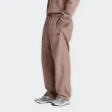 Pantalón deportivo New Balance de tejido técnico color marrón topo, con cintura elástica ajustable con cordón, bolsillos laterales con cierre y cordón de ajuste en el dobladillo. Presenta un pequeño logo gráfico en la pierna izquierda.