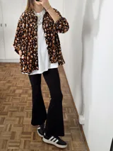 Sobrecamisa de plush con estampado animal print en tonos marrones, negros y blancos. Presenta cuello camisero, cierre frontal con botones, bolsillos laterales y mangas largas con puños. El diseño incluye un tajo en los laterales y un largo asimétrico, siendo más corta en la parte delantera.