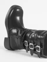 Botas negras de cuero sintético, con caña media, taco cuadrado y suela track. Presentan triple hebilla decorativa en la parte superior de la caña.