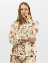 Conjunto de dos piezas compuesto por camisa de manga larga con cuello solapa y botones frontales, y pantalón de tiro alto con pierna recta y bolsillos laterales. Ambas prendas presentan un estampado paisajístico en tonos marrones sobre fondo crema.