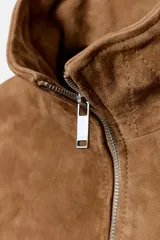Cazadora de ante 100% color tostado, con cuello alto ajustable mediante hebilla, cierre frontal de cremallera metálica, mangas largas con trabillas ajustables en los puños y bajo elástico.