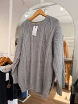 Sweater de tejido de punto grueso color gris, con diseño de trenzas en relieve, cuello redondo, mangas largas y terminaciones acanaladas en puños, cuello y cintura.