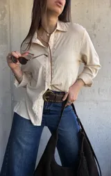 Camisa beige de manga larga con detalles bordados en la botonera y el cuello, cierre frontal con botones y diseño fluido.