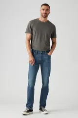 Jean de corte slim fit con tiro bajo, confeccionado en denim azul con efecto de lavado desgastado. Presenta cierre de botones y remaches metálicos clásicos.