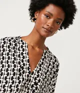Blusa de viscosa con estampado geométrico en blanco y negro, escote de pico, manga corta y bajo elástico.