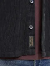 Sobrecamisa de manga larga confeccionada en pana de algodón, con cuello camisero, cierre frontal de botones, puños abotonados y un bolsillo en el pecho. Presenta un corte relajado y textura acanalada.