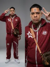 Conjunto deportivo de dos piezas en color bordó, compuesto por un buzo con cierre frontal y capucha, y un pantalón de jogging a juego. Ambas prendas presentan detalles estampados en blanco, incluyendo estrellas, logotipos circulares y tipografía cursiva.