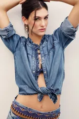 Camisa de denim de lyocell con cierre frontal de broches metálicos, cuello redondo con volados fruncidos y mangas largas con puños doblados.