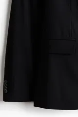 Blazer negro de corte entallado, confeccionado en tejido suave con solapas de muesca finas, un botón de cierre frontal, bolsillos con solapa y bolsillo superior en el pecho.