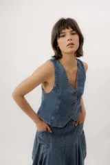 Chaleco de denim azul con cuello en V, cierre frontal con botones metálicos y pespuntes en contraste.