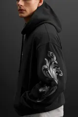 Hoodie negro oversize con estampado de cruz en el pecho y diseño floral en las mangas.