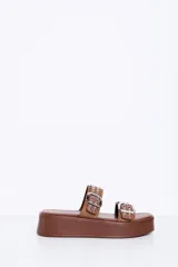 Sandalias de plataforma color marrón camel, con dos tiras en el empeine decoradas con hebillas metálicas plateadas y tachas. Suela plana y corrida.