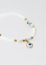Pulsera elastizada con mostacillas blancas y doradas, con dije colgante de ojo turco con borde color cobre.