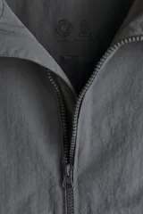 Campera rompevientos de nylon repelente al agua, con capucha ajustable, cierre frontal completo, bolsillos laterales y puños elásticos.