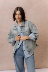 Campera de denim oversized en lavado celeste, con hombros caídos, cierre frontal con botones metálicos, bolsillos delanteros con tapa y aplicaciones de strass con diseño orgánico en delantero, mangas y espalda.