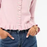 Cárdigan de punto color rosa, con cuello redondo, cierre frontal de botones y detalles de volados en la tapeta, el ruedo y los puños.