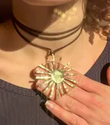 Collar con dije dorado en forma de sol con rayos texturizados y cordón negro.