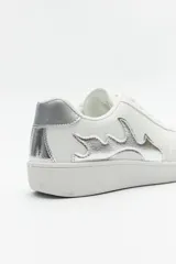 Zapatilla urbana de cuero sintético color blanco, con diseño de llamas plateadas en el lateral y detalle metalizado en el talón. Cuenta con cordones al tono y suela de goma.