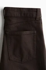 Jean de cinco bolsillos, tiro alto, color marrón oscuro, con piernas anchas y rectas. Cierre frontal con botón.
