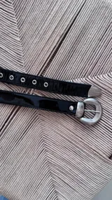 Cinto de cuero negro con textura gamuzada, presenta una hebilla metálica plateada de diseño redondeado con detalles grabados y pasador metálico a juego.
