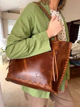 Cartera tipo shopper de cuero genuino color marrón con estampado texturado tipo cocodrilo. Presenta detalles de costuras y tiras trenzadas artesanales en los bordes y en las asas de hombro.