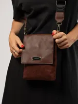 Bandolera de diseño compacto en color verde oliva, confeccionada en material símil cuero con detalles en textura tipo gamuza. Cuenta con solapa frontal, placa metálica con logo de la marca y correa ajustable de cinta negra con el nombre de la marca grabado.