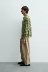 Camisa de corte relajado confeccionada en tejido de algodón con estampado de cuadros en tonos verdes y beige. Presenta cuello solapa, cierre frontal con botones a presión, bolsillos plastrón en el pecho y mangas largas con puños abotonados.