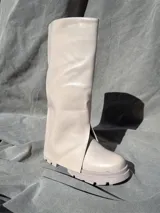 Bota de caña alta color blanco de cuero sintético con suela track y abertura lateral.