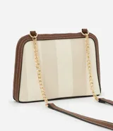 Cartera bandolera pequeña con estampado de rayas verticales en tonos beige y blanco, con detalles en marrón. Tiene cierre de cremallera, asa de cadena dorada y correa de cuero sintético marrón.