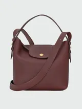 Cartera bucket de cuero marrón texturizado, con solapa frontal con cierre de botón a presión metálico dorado, asa corta superior y correa cruzada ajustable.