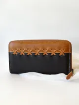Billetera grande de cuero color negro y camel, con cierre metálico y detalle de costuras cruzadas en la parte superior. Incluye monedero interno.