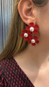 Aros colgantes de diseño floral en color rojo mate, compuestos por tres flores unidas en una estructura circular, cada una con una perla central.
