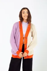 Cárdigan tejido de punto con diseño color block en lila, beige y naranja. Tiene cuello en V, cierre con botones de madera y bolsillos frontales.