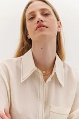 Camisa color crema de lyocell con cuello clásico, cierre frontal con botones, bolsillo de parche en el pecho y pespuntes a contraste en negro.