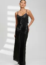 Vestido largo de fiesta color negro con acabado metalizado y diseño plisado en toda la prenda. Presenta breteles finos, escote redondo y un detalle de fruncido central que crea un efecto visual dinámico en la silueta.