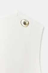 Chaleco de denim blanco, cruzado, sin mangas, con cuello redondo, detalle de cinturón fino con hebilla dorada en la cintura y cierre de botón dorado en el hombro.