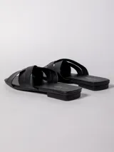 Sandalia baja negra de cuero sintético, con tiras anchas cruzadas en el empeine y suela plana.