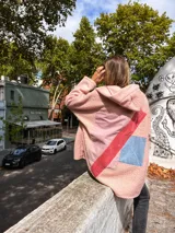 Campera de corderito sintético en color rosa, con diseño de collage en la espalda que incorpora parches de tela en tonos rosa, rojo y azul. Presenta capucha, cierre frontal y un corte holgado y cómodo.