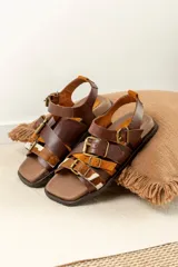 Sandalias de cuero marrón con diseño de tiras múltiples, hebillas metálicas ajustables y detalle de cuero con pelo estampado en la parte frontal. Presentan una base cuadrada y cierre de pulsera en el tobillo.
