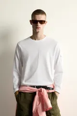 Camiseta de manga larga con cuello redondo y corte relajado. Presenta un pequeño bolsillo tipo plastrón con solapa en la manga izquierda.