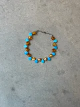 Gargantilla corta hecha a mano con mix de cuentas de cristal en forma de gota, alternando tonos celestes y ámbar, con terminaciones y cadena de extensión en acero.