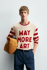 Camiseta de manga larga con cuello redondo, cuerpo color beige claro y mangas a rayas horizontales rojas y beige. Presenta texto frontal en relieve color rojo que dice "WAY MORE ART".