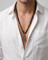 Collar de cuentas esféricas de ónix negro mate y ojo de tigre, con dije central de acero en forma de punta de flecha.