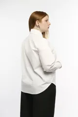 Camisa oversize de manga larga en color blanco, confeccionada en algodón. Presenta cuello clásico, puños abotonados y una abertura central ovalada con jaretas ajustables que permiten fruncir la prenda.